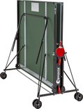 Een groene tafeltennistafel, ingeklapt en op wieltjes, met een metalen frame. De onderkant is zwart.