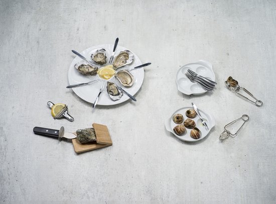 Een oestermes, citroen en een servies met oesters en slakken op een betonnen ondergrond.