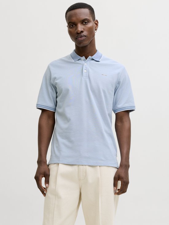 Man in lichtblauw poloshirt met witte kraag en manchetten, beige broek.