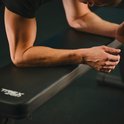 Gedetailleerde opname van de armen van een man die op een zwarte trainingsbank rust.