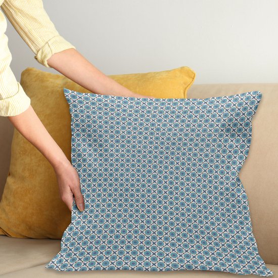Een blauw kussen met een repetitief geometrisch patroon van blauwe cirkels met witte stippen en vierkante vormen, geplaatst op een bank naast een geel kussen.