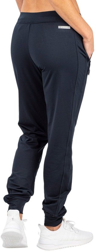 Vrouw in donkerblauwe sportbroek, achterkant met ritssluiting en sneakers.