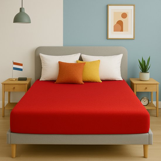 Un drap-housse rouge est tendu sur un lit avec deux tables de chevet, des coussins et de la décoration.