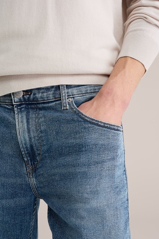 Close-up van een blauwe jeans met lichte wassing, met een hand in de zak.