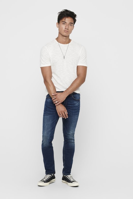 Man in donkerblauwe skinny jeans, wit t-shirt en zwarte sneakers, van voren gezien.