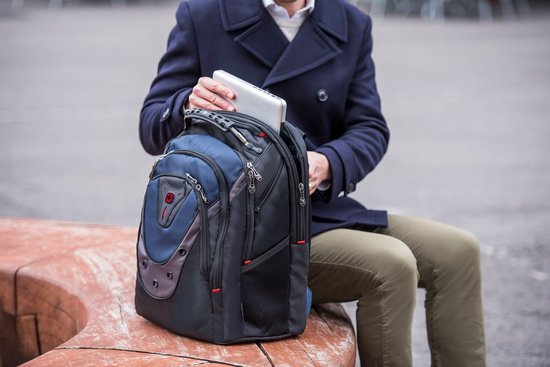 Man in donkerblauwe jas plaatst een laptop in een zwarte rugzak met blauwe en grijze vlakken.
