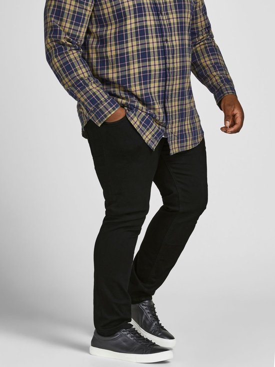 Man in een geruite blouse en zwarte jeans, hand in de zak.