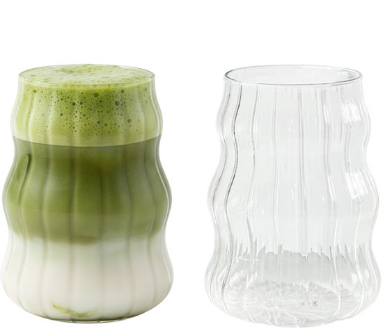 À côté d'un verre côtelé vide se trouve un verre rempli de matcha latte.