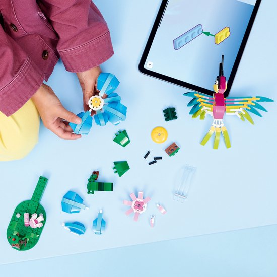 Des mains d'enfants construisent avec des briques LEGO, avec une fleur bleue, une fleur rose et un colibri en construction.