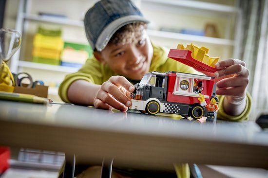 Kind bouwt LEGO snackbartruck. Rode truck met frietjes, poppetjes en een tablet met bouwinstructies.
