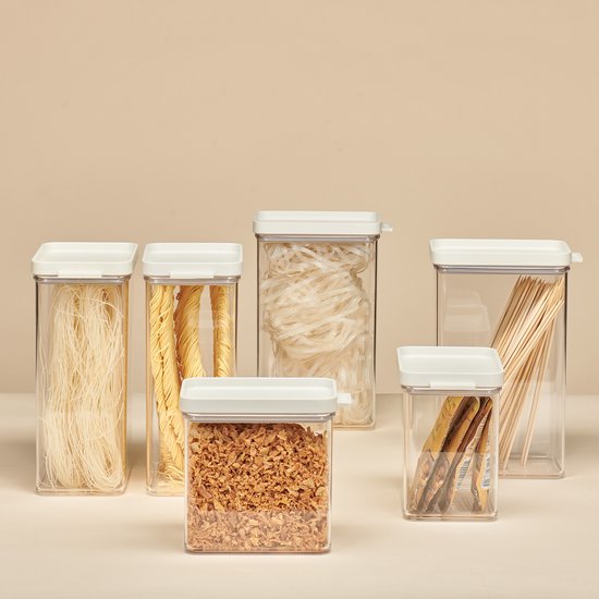Six boîtes de conservation transparentes remplies de diverses pâtes, riz, oignons frits et bâtonnets en bois. Toutes avec des couvercles blancs.
