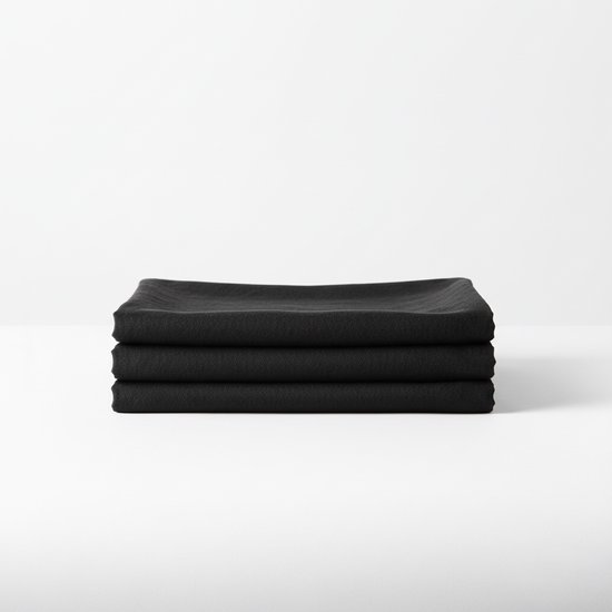 Pile de trois nappes noires pliées à texture fine sur fond blanc.