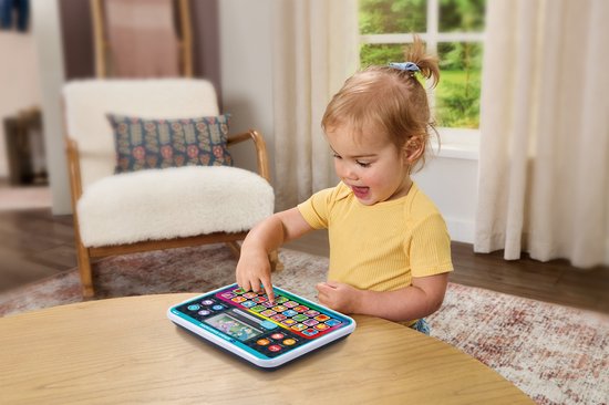 Een meisje met een geel shirt speelt met een blauwgroen alfabet Kindertablet op een houten tafel.