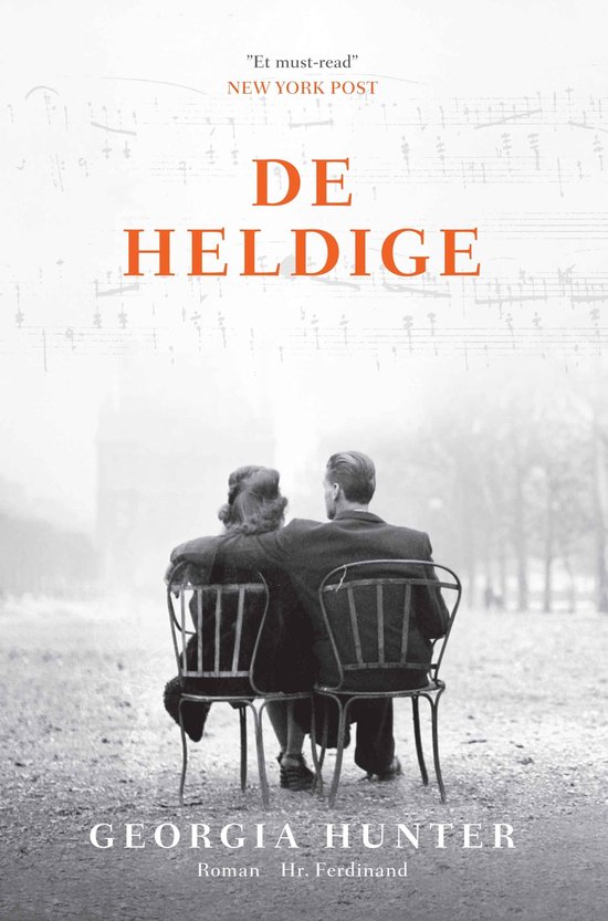 Boek 'De Heldig' van Georgia Hunter met op de voorkant een stel dat op stoelen zit te kijken naar muzieknoten.
