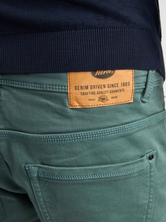 Detail van het leren label met merklogo 'Petrol Industries' op een groene slim fit stretch denim shorts.