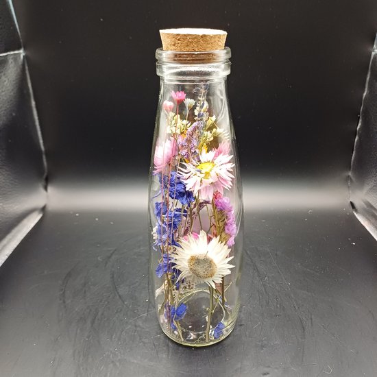 Glazen fles met kurk, gevuld met gedroogde bloemen in roze, paars, wit en blauw.