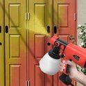 Hand houdt rode verfspuit, spuit gele verf op een oranje/geel geverfde deur.
