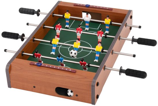 Mini voetbaltafel met groen speelveld, houten frame, rode, blauwe en witte spelers. Een bal ligt op het veld.