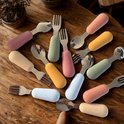 Gouden roestvrijstalen bestek met gekleurde handvatten in roze, pastelgeel, oranje, groen en blauw op een houten tafel.