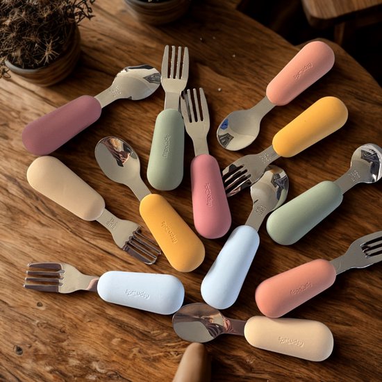 Gouden roestvrijstalen bestek met gekleurde handvatten in roze, pastelgeel, oranje, groen en blauw op een houten tafel.