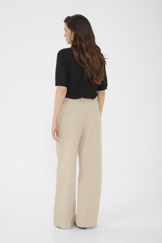 Model van achteren gezien, in een zwarte top en een beige wijde broek.