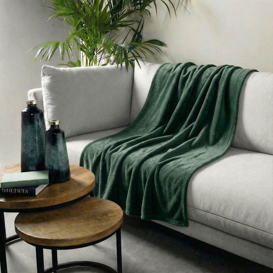 Een donkergroen fleece plaid is gedrapeerd over een witte bank, naast twee decoratieve vazen.