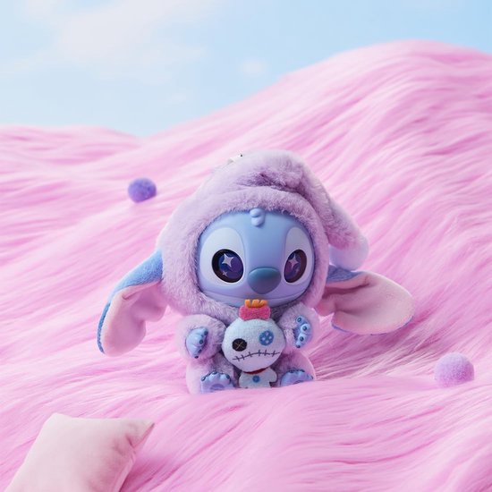 Een paarse Stitch pluche speelgoedje in slaapmutsje, met een voodoo-pop in de handen, op roze heuvels.