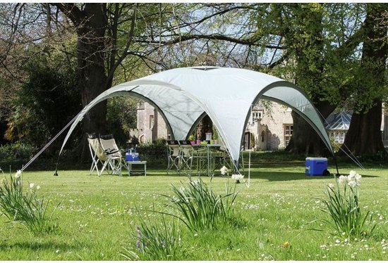 Een Coleman partytent in een weelderige tuin, met een gebouw op de achtergrond.