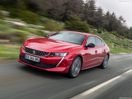 Rode Peugeot 508 sedan die rijdt op een bochtige weg in een bosrijke omgeving.