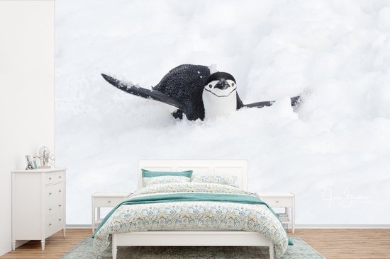 Behang - Fotobehang Een pinguïn glijdt op zijn buik door de sneeuw - Breedte 450 cm x hoogte 300 cm