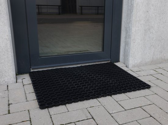 Zwarte ringmat met open structuur, bij de ingang van een gebouw.