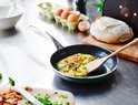 Een omelet wordt gebakken in een koekenpan op een roestvrijstalen aanrecht, met ingrediënten.
