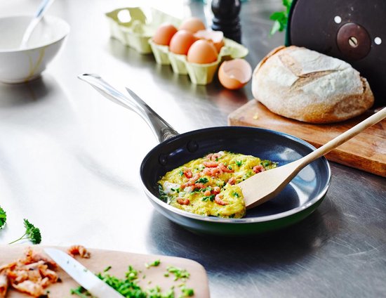 Een omelet wordt gebakken in een koekenpan op een roestvrijstalen aanrecht, met ingrediënten.