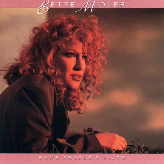 Bette Midler met rood, krullend haar, kijkt weg van de camera, gekleed in een bruin jasje.