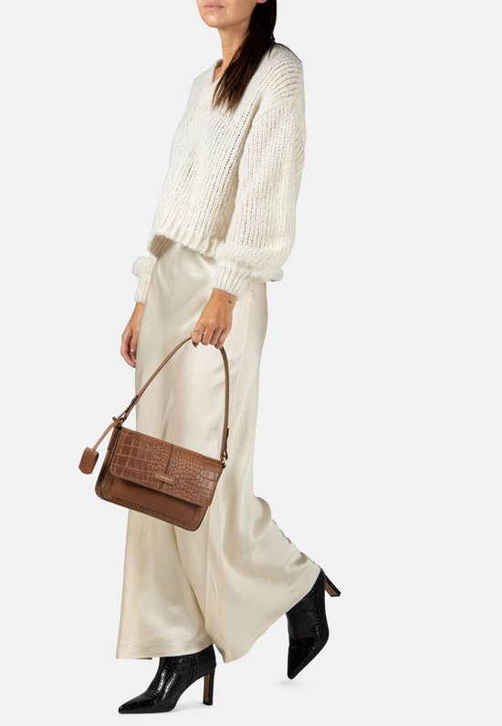 Vrouw met een witte trui, beige rok en zwarte laarzen, met een bruine schoudertas.