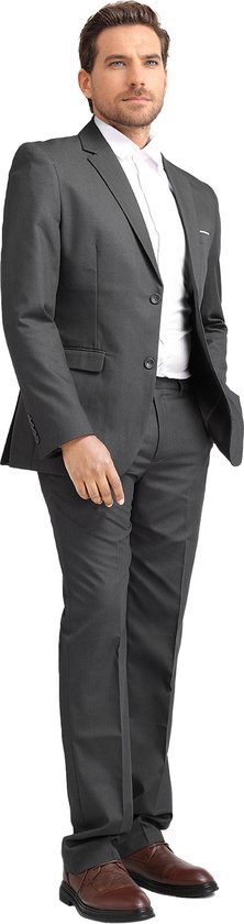 Man in donkergrijs slim fit pak met wit overhemd, staand, met hand in broekzak.