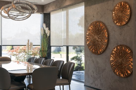 Eetkamer met tafel, stoelen, witte en beige rolgordijnen, en gouden wanddecoratie.