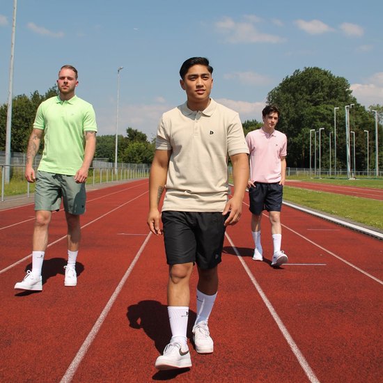 Drie mannen op een atletiekbaan, twee met poloshirts aan. Een man in het midden draagt een beige poloshirt met korte mouwen en een zwarte short.