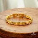 Gouden schakelarmband met dubbele rij schakels en rechthoekige gesp, op houten ondergrond.