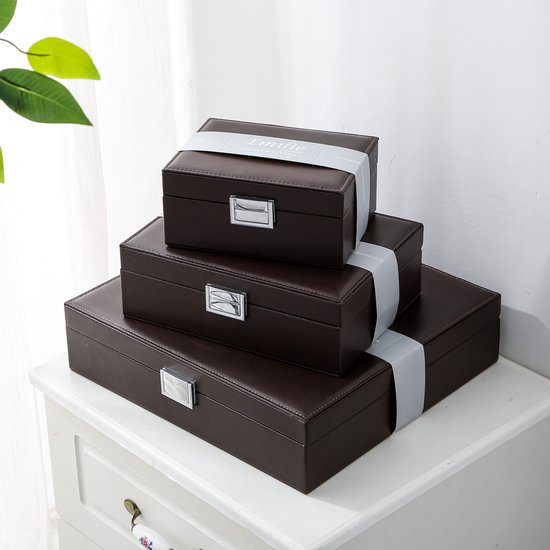 Drie bruine opbergdozen van Emilie Collection opgestapeld, met linten, op een witte commode.