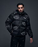 Model in zwarte puffer jas met capuchon, witte wolkenprint en opstaande kraag.