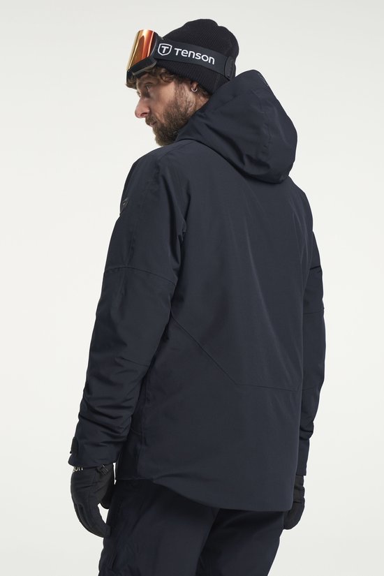 Homme portant une veste de ski Tenson foncée, regardant par-dessus son épaule. Bonnet noir avec logo.