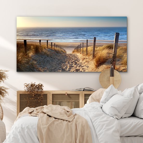 Un sentier à travers les dunes, bordé d'herbes, mène à la mer au coucher du soleil.