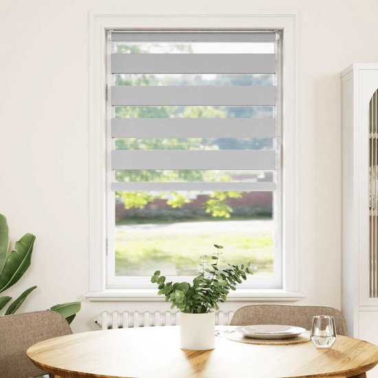 Grijs rolgordijn met horizontale banen hangt voor een raam in een woonkamer.