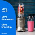 Zilverkleurige Nutribullet blender met een volle blendbeker met fruit en een glas met roze smoothie.