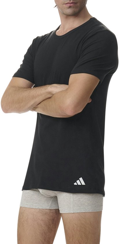 Man in zwart Adidas T-shirt en grijze boxershort, met armen over elkaar.