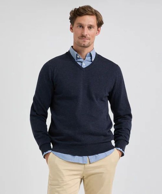 Man in een casual outfit met een marineblauwe V-hals trui, lichtblauw overhemd en beige broek.