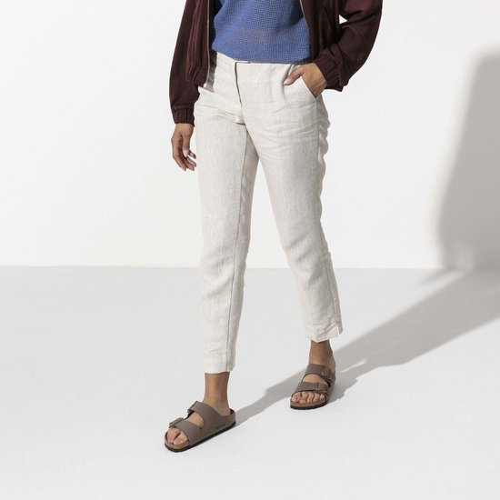 Vrouw met bruine Birkenstock Arizona slippers, beige broek en bordeaux jasje.