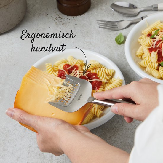 Des mains râpent un bloc de fromage avec une râpe à fromage argentée à poignée ergonomique au-dessus d'une assiette de pâtes.