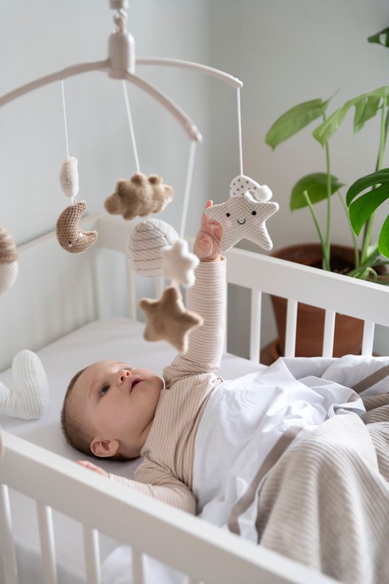 Baby in een ledikantje met een mobiel met gebreide sterren en manen.